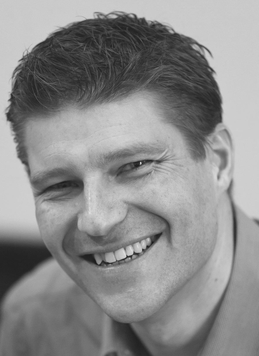schwarz-weißes Porträtfoto eines jungen Mannes, der in die Kamera lächelt