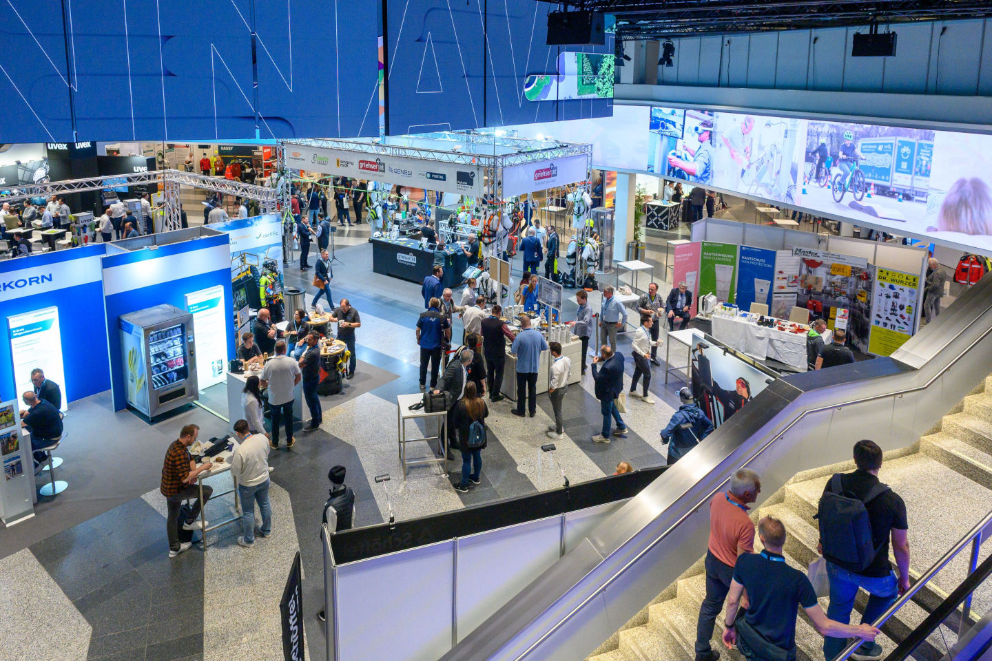 Messehalle mit diversen Ständen und vielen Besucher:innen