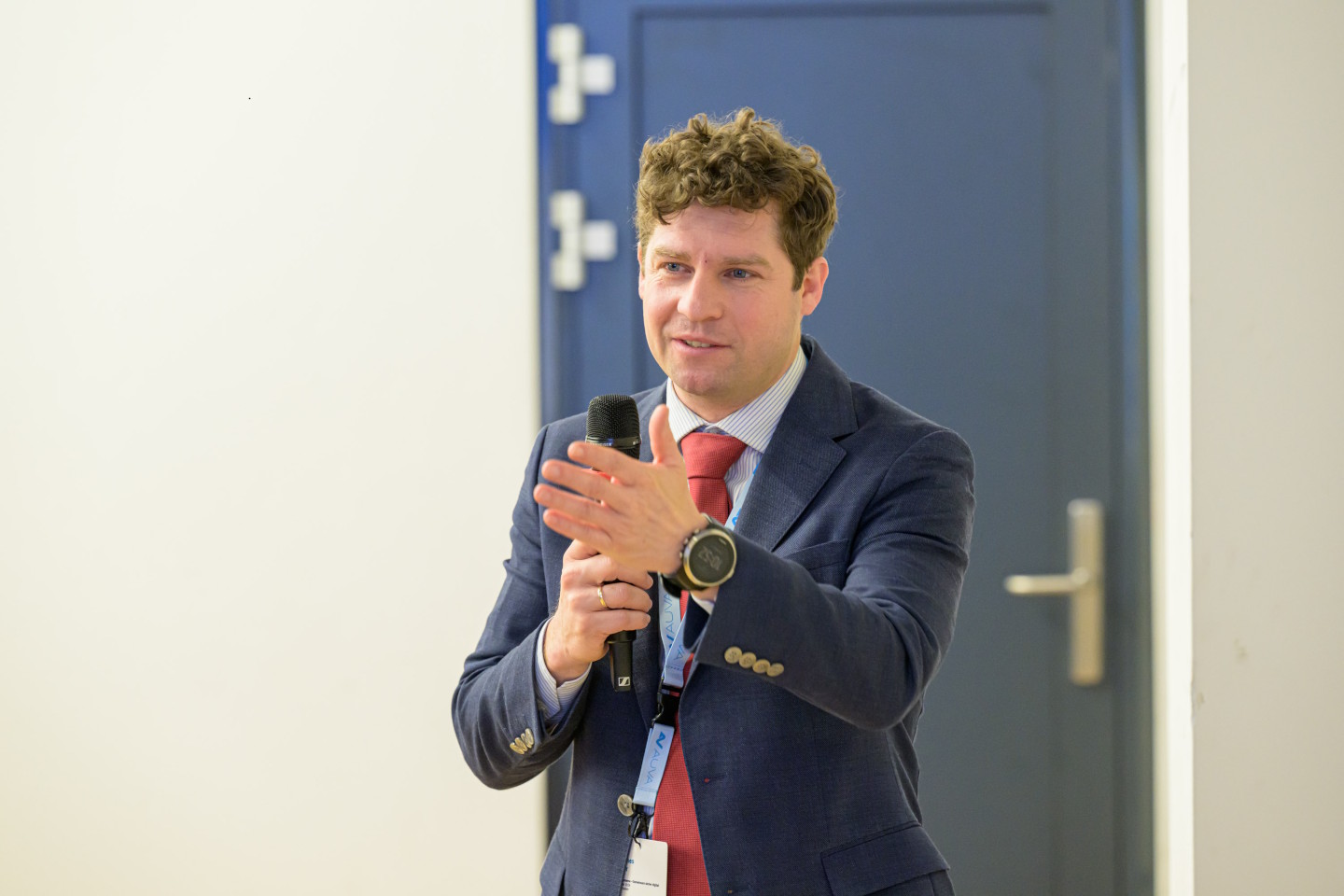 Dr. Johannes Warter spricht mit einem Mikro in der Hand vor einer blauen Tür