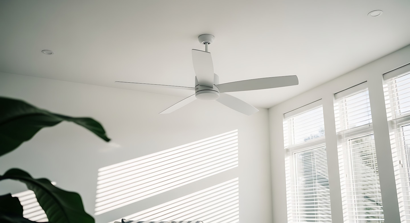 Ein weißer Deckenventilator hängt in einem Innenraum, dessen Fenster halb geöffnete Jalousien zeigen.