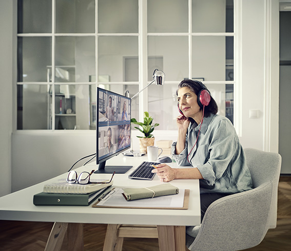 Frau mittleren Alters sitzt vor einem Computer und hat rote Kopfhörer auf.