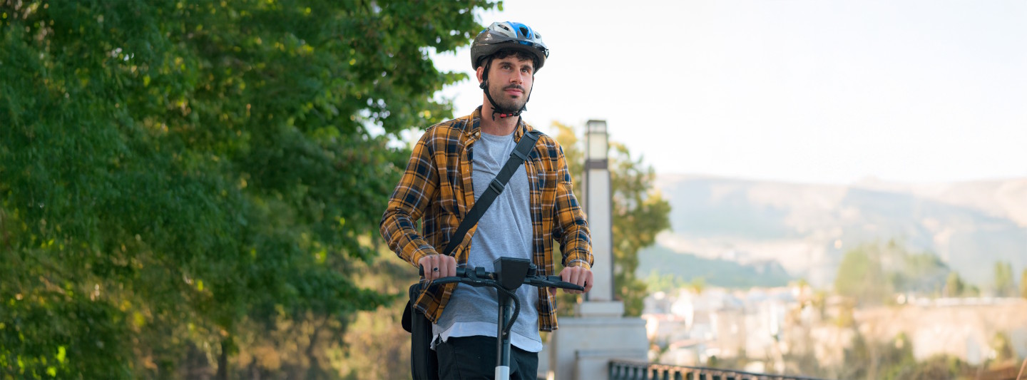 Junger Mann mit Helm auf einem E-Scooter
