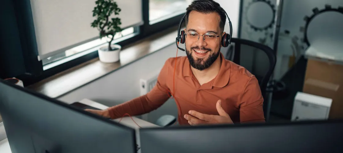 Adobestock 1136791538 1440 ©Zamrznuti Tonovi WEB Mann mit Headset sitzt vor zwei Bildschirmen