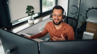 Adobestock 1136791538 1440 ©Zamrznuti Tonovi WEB Mann mit Headset sitzt vor zwei Bildschirmen