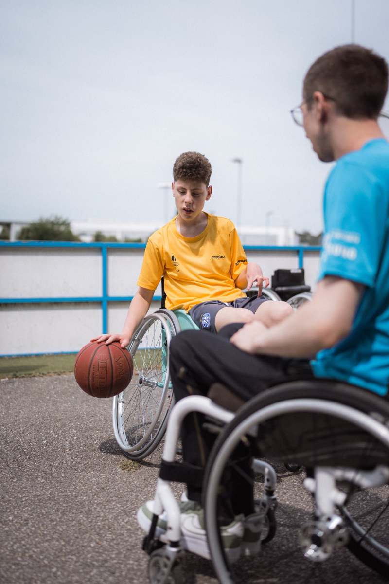 Szene beim Rohlstuhlbasketball: Junge dribbelt mit dem Ball, sein erwachsener Gegenspieler ist auch im Bild