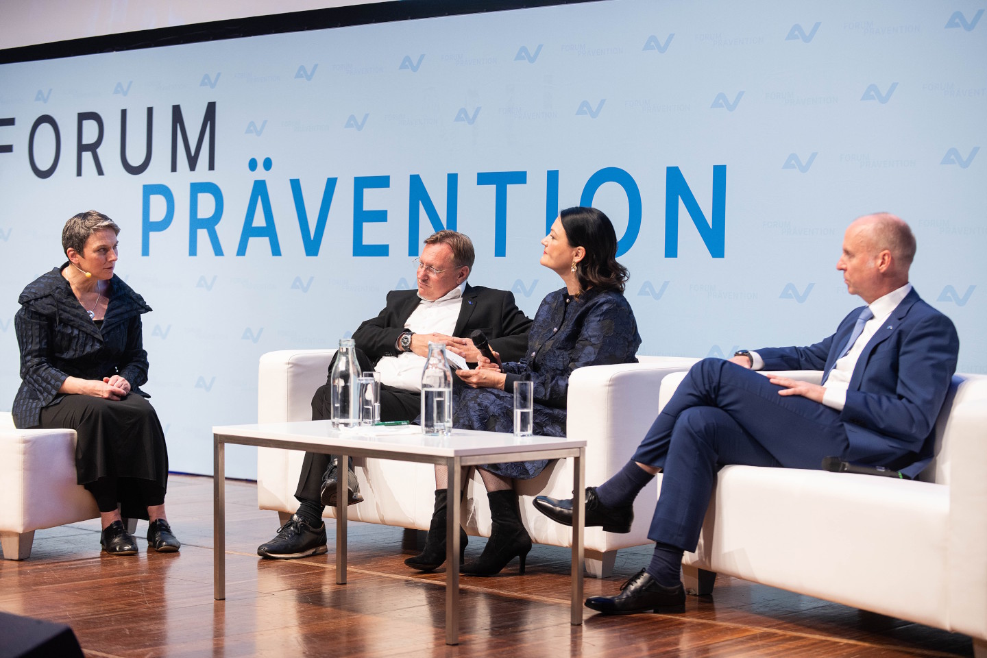 Vier Menschen sitzen bei einer Podiumsdiskussion auf weißen Sofas auf der Bühne des Forum Prävention