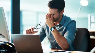 Mann bei der Bildschirmarbeit. Seine Augen tun ihm sichtlich weh.