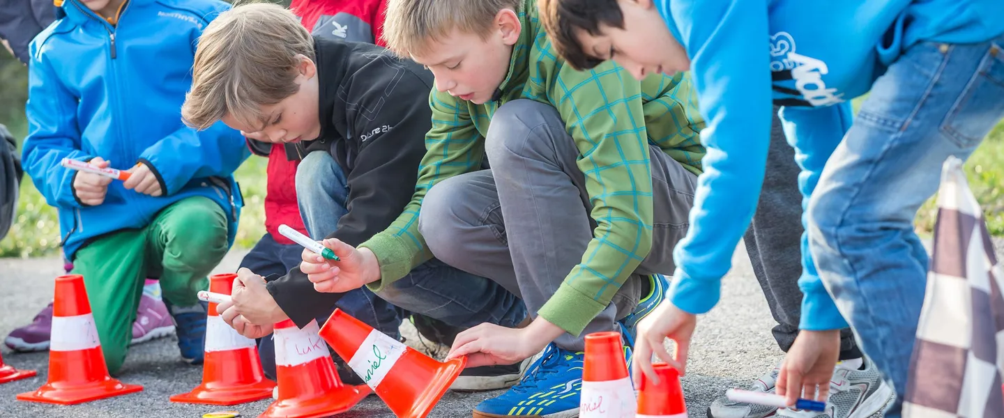 Fünf Buben im Volksschulalter lernen an einem Verkehrsübungsplatz anhand von Leitkegeln über den Bremsweg und Anhalteweg von Autos.