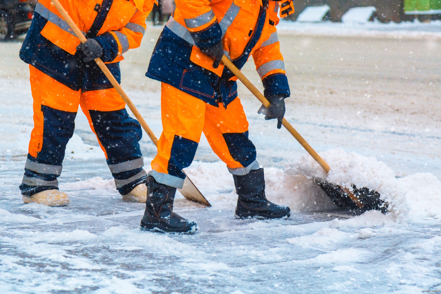 zwei Menschen in winterlicher Warnkleidung beim Schneeschaufeln