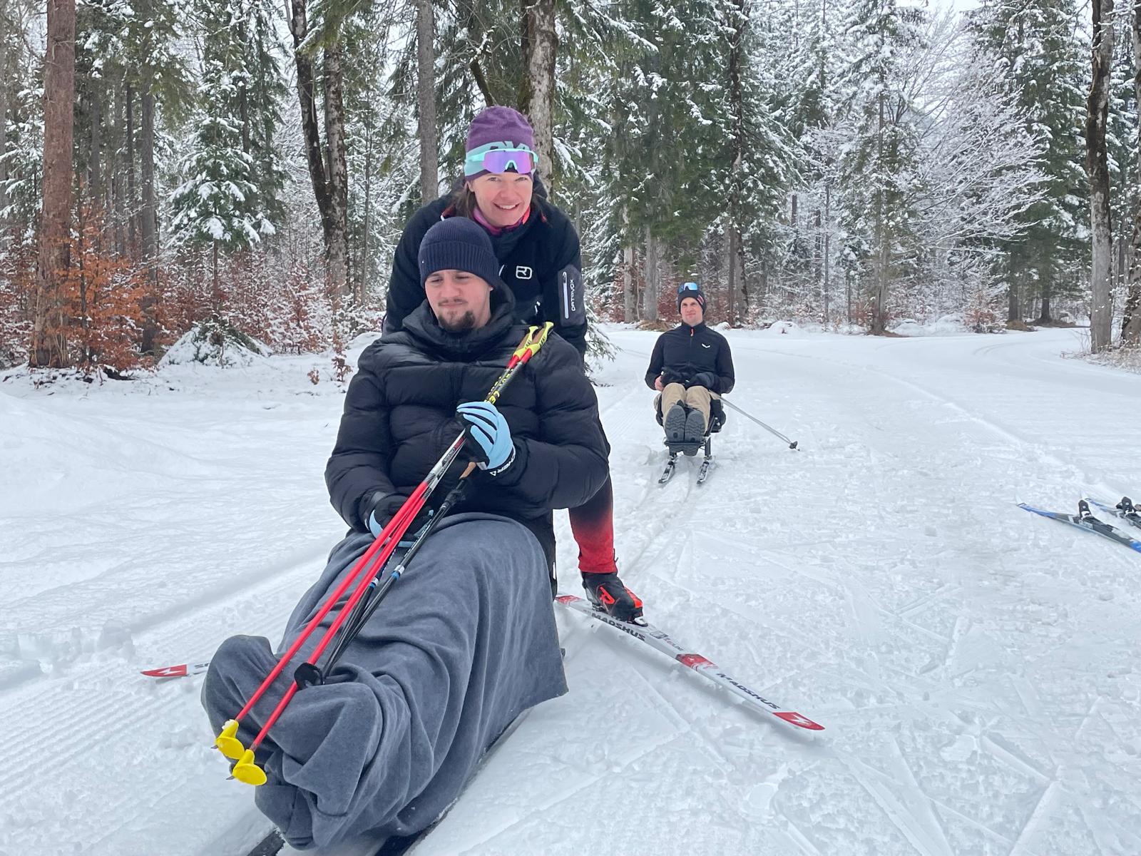 Zwei Teilnehmende des Trainings in Aktion mit Langlaufschlitten, im Bild ist außerdem die Trainerin zu sehen