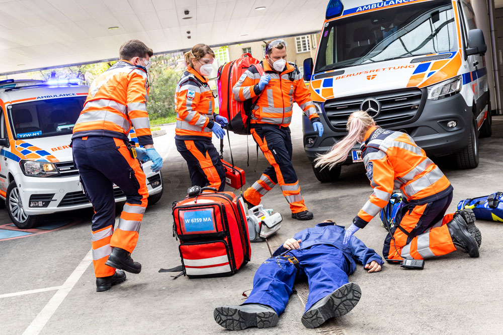 Sanitäter:innen bei Einsatz-Übung mit Notarzt-Einsatz-Fahrzeug (NEF) im Hintergrund