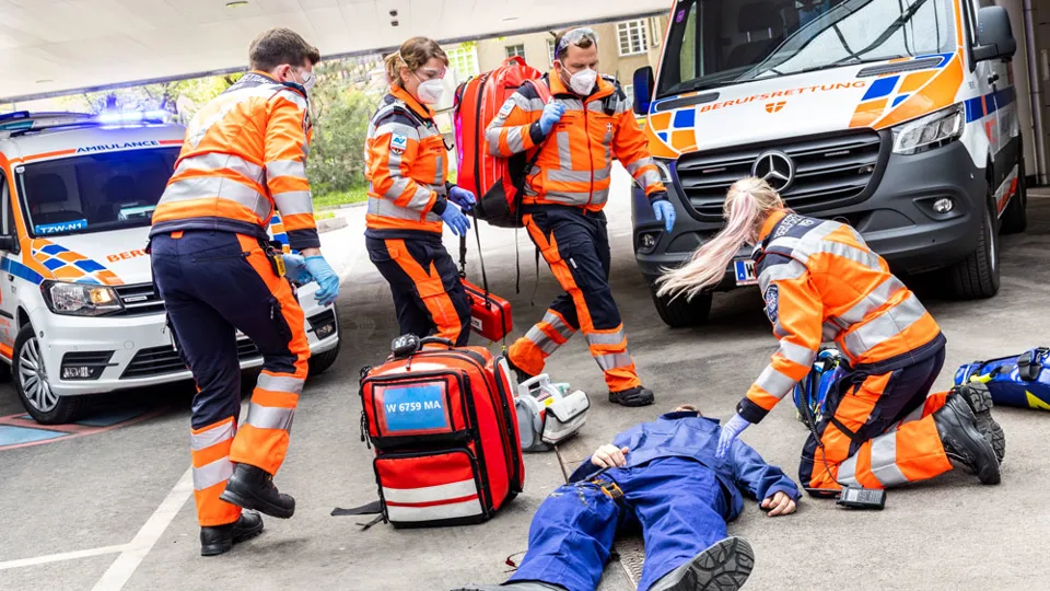 Sanitäter:innen bei Einsatz-Übung mit Notarzt-Einsatz-Fahrzeug (NEF) im Hintergrund