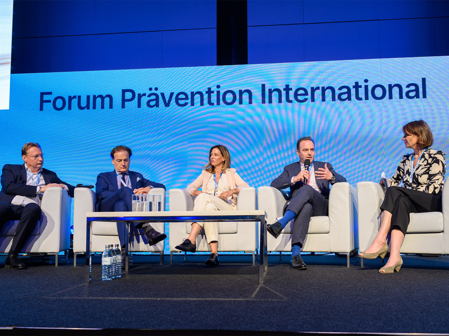 Fünf Personen sitzen auf Stühlen am Podium. Im Hintergrund steht "Forum Prävention International"