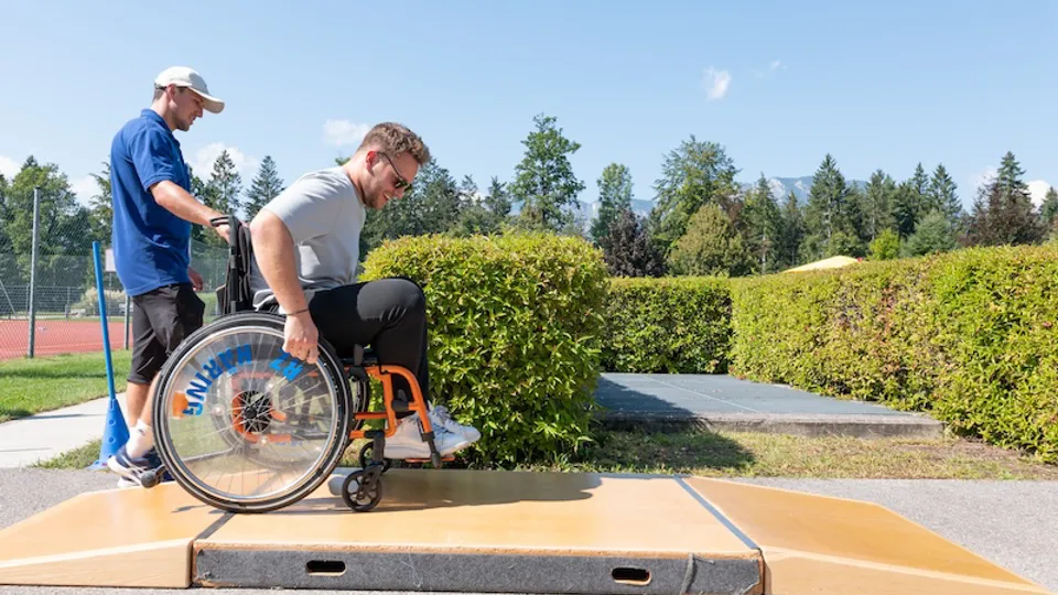 Ein Patient mit einem Mitarbeiter des Rehazentrums beim Rollstuhltraining in den Außenanlagen des Rehazentrums.
