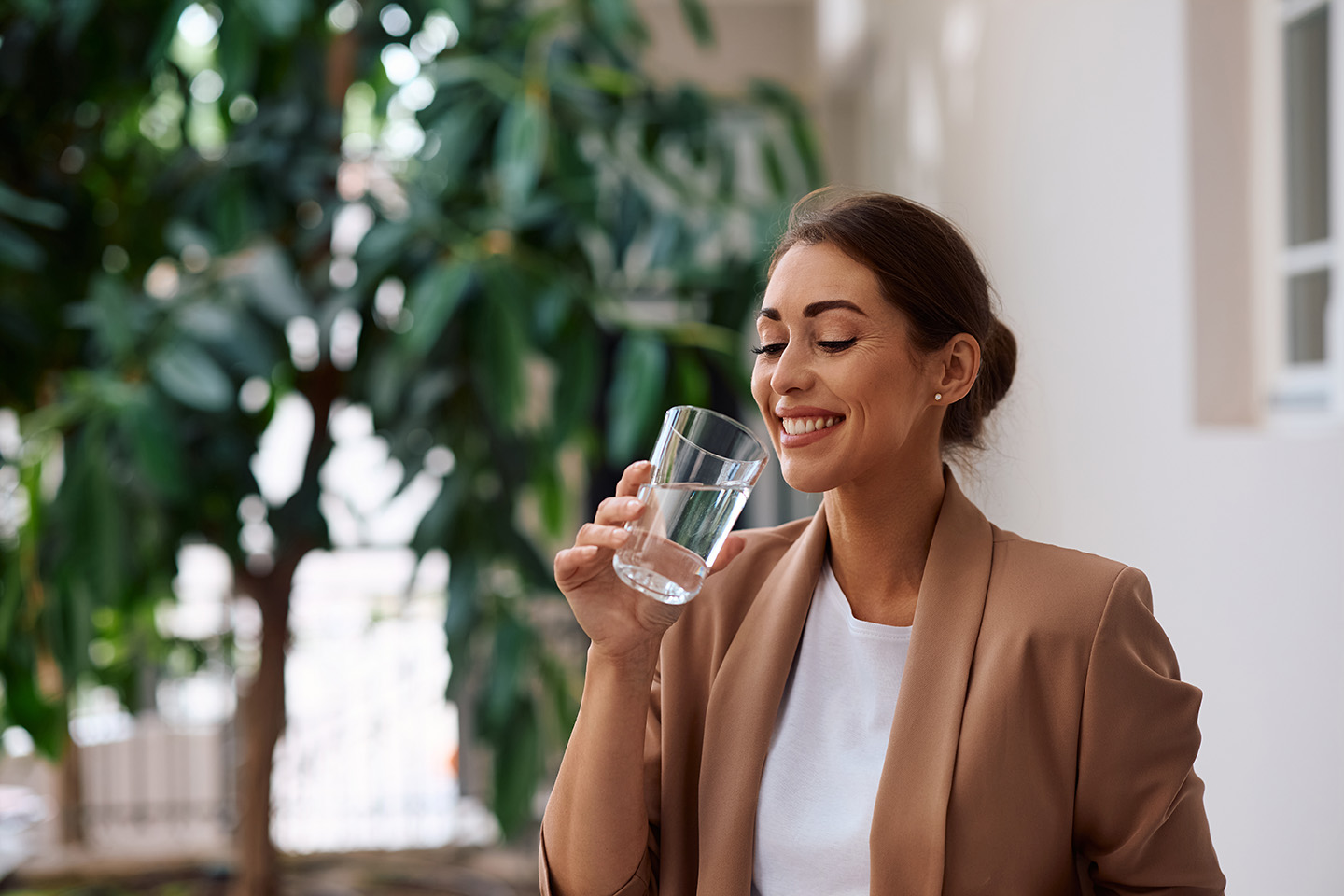 Eine junge Frau im Businessoutfit trinkt ein Glas Wasser