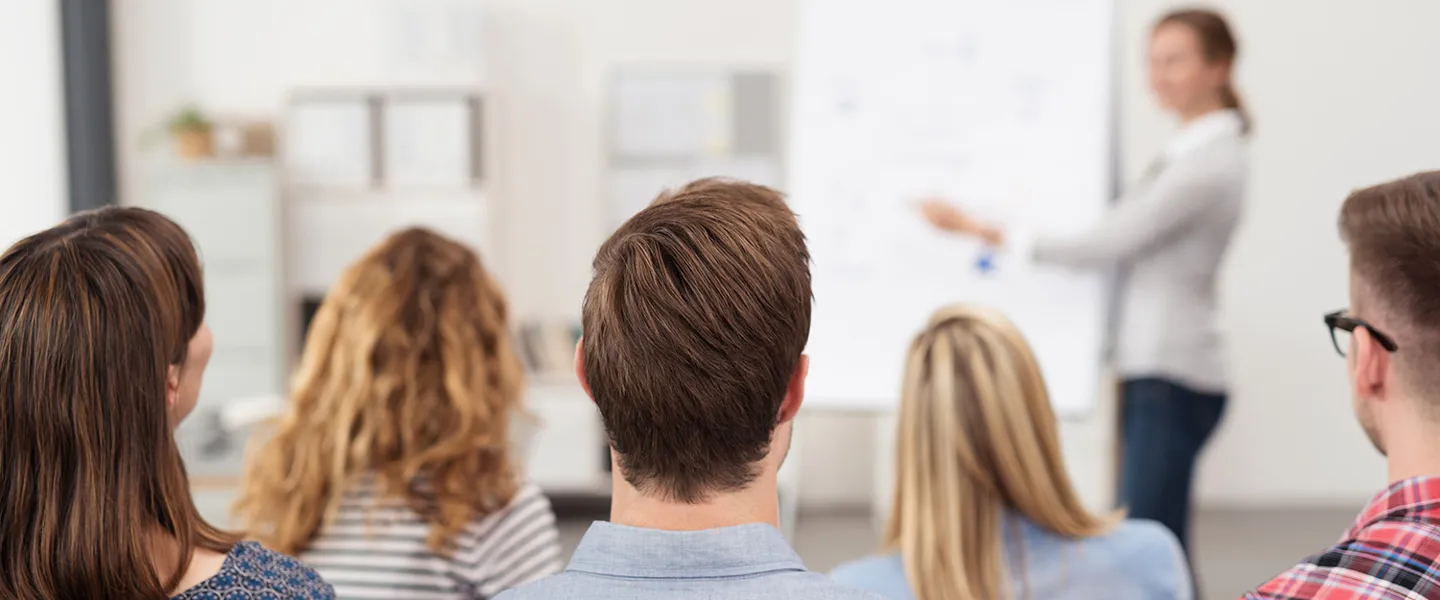 4.3_Schulungen_Veranstaltungen_AdobeStock_86512117.jpeg Seminarteilnehmer hören aufmerksam der Fachexpertin zu, die am Flipchart erklärt.