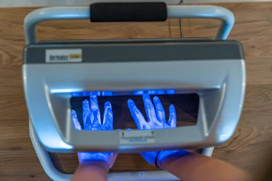 Ein Gerät mit UV-Licht zeigt, an welchen Stellen die Hände einer Person schlecht eingecremt wurden.
