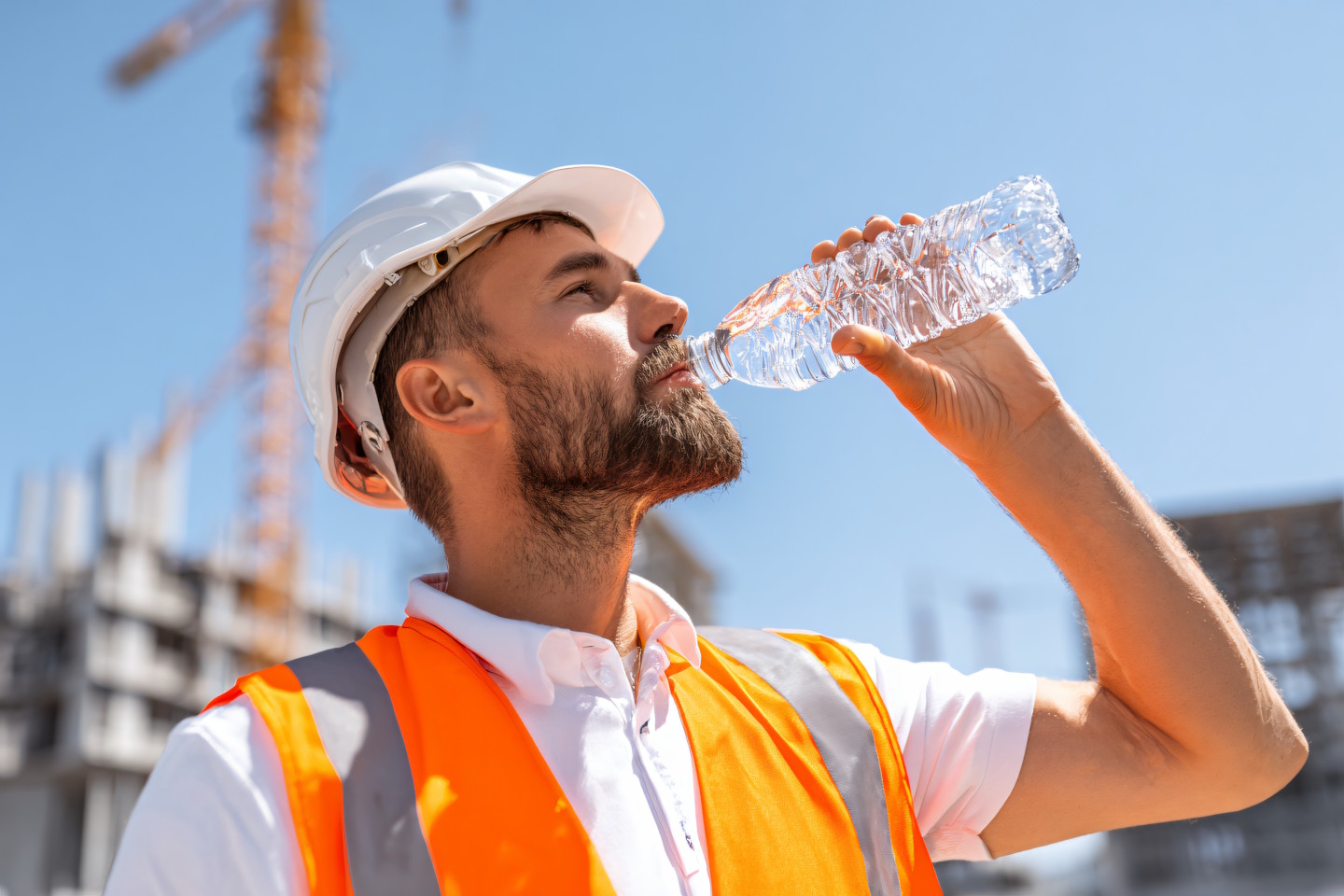 Ein Bauarbeiter auf einer Sommer-Baustelle trinkt aus einer Wasserflasche.