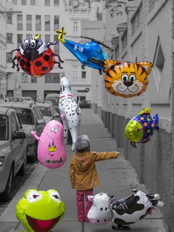 Ein Kind mit mehreren Ballons geht die Straße entlang.