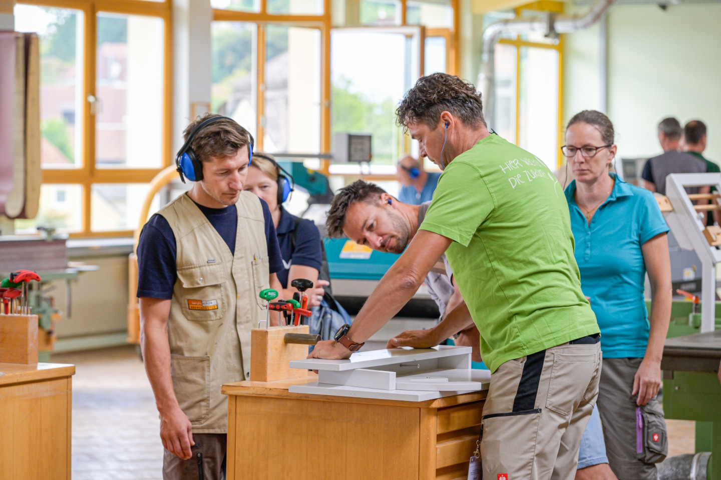 drei Erwachsene beim Arbeiten an einer Holzkreissäge