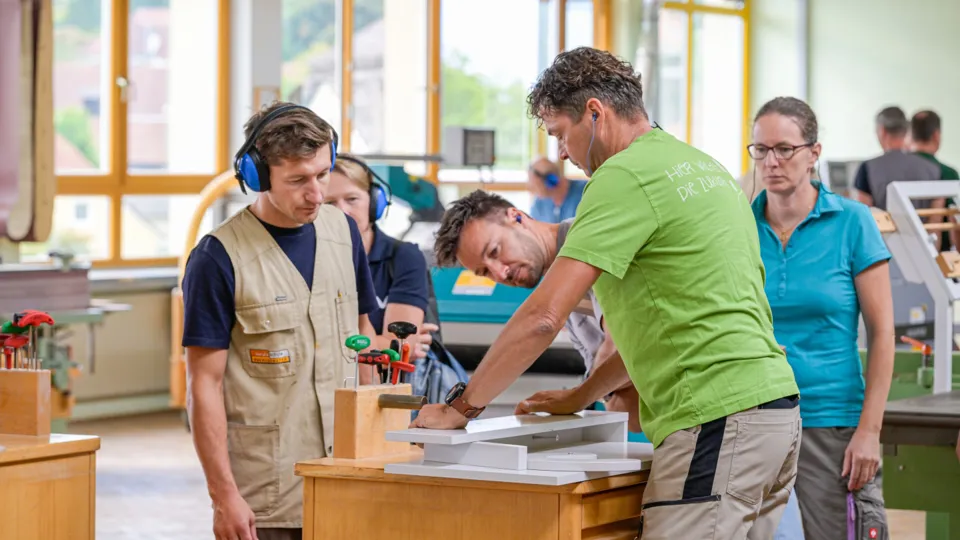 drei Erwachsene beim Arbeiten an einer Holzkreissäge