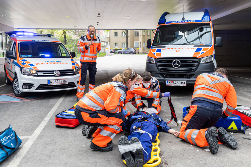 Sanitäter:innen bei Einsatz-Übung mit Notarzt-Einsatz-Fahrzeug (NEF) im Hintergrund